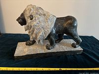 Side view of the soapstone lion sculpture showing the contrasting textured mane and polished body with measuring tape indicating approximate length.