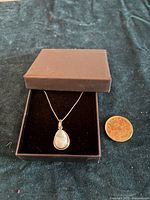 Photo of the pendant necklace in black box alongside a coin for size reference.