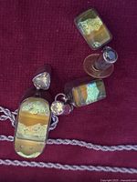 Closeup photo of sterling silver pendant, earrings and chain arranged on a purple surface showing colorful layered stones and metal detail.