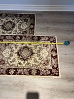 Both small wool rugs laid flat with measuring tape showing length difference.