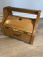 Closed vintage wooden KIWI shoe shine box with handle on top and hinges on front closing the lid.