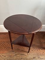 Front top view of dark wood oval side table with drop leaves and polished surface.