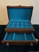 Open wooden jewelry box showing turquoise velvet-lined compartments and removable tray with multiple sections.