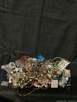 Lot of mixed custom jewelry arranged on black fabric, showing the assortment of beaded, metal, and feather elements.