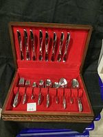 Full view of the open wooden flatware box displaying knives on the lid and assorted forks and spoons arranged on the base with red fabric lining.