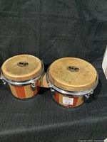 Pair of MP bongo drums connected, showing wooden shells with striped pattern and natural skin drum heads with MP logo.