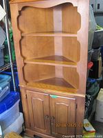 Front view of the wooden corner hutch showing two open shelves and lower cabinet with double doors.