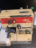 Front and left side view showing the Elna Lock L5 serger sewing machine with tension dials and threading visible.