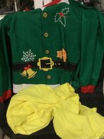 Front view of large green elf costume tunic with yellow pants, showing printed holiday decorations and belt design