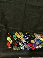 Photo showing 21 assorted toy cars including race cars, military, trucks, and vintage style vehicles in varied colors and manufacturers.