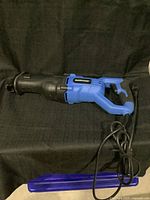 Full view of the Mastercraft electric reciprocating saw, blue and black color, with attached power cord and blue case placed next to it.
