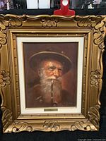 Front view of the original oil painting in an ornate gold frame showing the elderly man with a pipe.