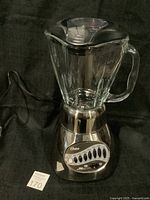 Full view of the Oster 16 Speed Blender showing the glass pitcher on top of the black and stainless steel base with control buttons and power cord.