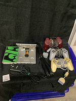 PlayStation 1 console open showing disc tray, four controllers coiled up, power adapter, AV cables, and a green flaming design booklet on black background.