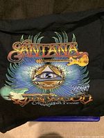Front graphic of the Santana black T-shirt with colorful design and 2010 text.