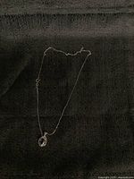 Full view of the necklace laid on black fabric, showing the chain and pendant.