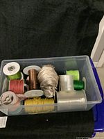 Plastic container holding multiple spools of thread in different colors and a bundle of string inside.