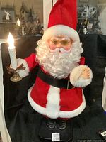 Front view of a vintage style Santa Claus figurine wearing red and white suit holding a lit candle.