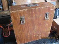 Closed view of vintage wooden record box showing metal latch clasps and handle on top, scratches and wear visible on surface.