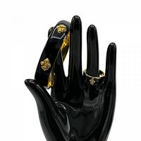 Black glossy mannequin hand displaying gold plated black enamel bracelet and matching ring with fleur de lis details.