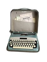 Typewriter in open case showing manuals in pocket, beige keys and blue-green enamel body with visible wear.