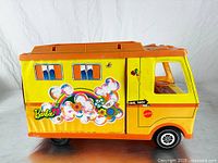 Yellow plastic Barbie camper vehicle with large colorful floral and rainbow decals, orange pop-up fabric roof, and illustrated interior visible through open sliding door.