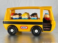 Side view of yellow Little Tikes school bus with 7 Toddle Tots figures inside. Bus shows Little Tikes logo and black stripe on body, with wheels and interior seating visible.