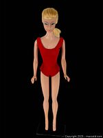 Front view of Barbie doll standing on display stand wearing red swimsuit with lemon blonde ponytail hair.