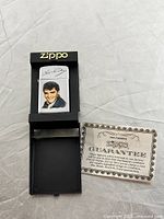 Front view of Zippo lighter in original black plastic case with Zippo logo, includes guarantee card
