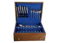 Opened wooden case displaying vintage flatware including knives, forks, and spoons inside blue fabric slots.