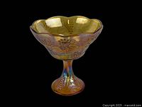Side view showing the full profile and pedestal of the marigold amber carnival glass bowl with grapevine decoration.