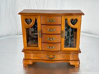 Front view of vintage wooden jewelry box with decorative metal handles and heart-shaped cutouts on glass doors
