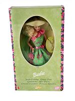 Front of green box with oval window showing Barbie doll wearing floral green dress and pink accessories, charm bracelet visible.