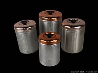 Full set of four vintage spun aluminum canisters with copper lids and black knobs, labeled Coffee, Sugar, Tea, and Flour, shown on black background.