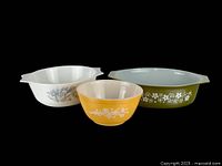 Three vintage Pyrex casserole and mixing bowls shown together on black background, displaying color and pattern variations in the set.
