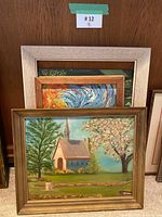 Front view of four stacked framed paintings, showing church scene, impasto horse painting and white frame landscape partially