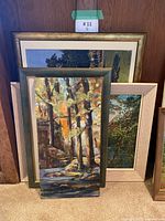 Four framed canvas paintings stacked against wall, front view