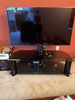 Front view of 55" Sony TV on three-tier glass stand with remote and cables visible on top shelf