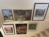 Six framed posters arranged in two rows of three on stairway wall. Various artists and galleries represented.