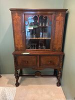 Front view of antique china cabinet showing wood carvings, glass doors, drawers, and turned legs.