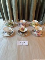 Six bone china tea cups and saucers arranged in two rows, each with unique floral patterns and gold trim. Photo taken to show full lot and designs.