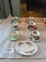 Overview of the tea cup sets with floral and playing card designs including plate, all set on paper with lot number.