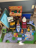 Overview of the lot showing wooden kids workbench, multiple toy vehicles, green chalkboard, Connect 4 and other small toys on a road-pattern rug