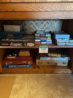 Wooden shelf with board games Scrabble, Life, Backgammon, and assorted playing card decks in plastic boxes