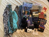 Photo showing an assortment of scarves, wallets, and small accessories arranged on a surface including items in plastic wrapping and boxes.