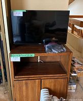 Front view of Samsung TV on wooden cabinet with an accessory cable in front.
