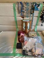 Six necklaces draped over upholstery with wood jewelry box beneath