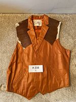 Front view of the brown leather vest with cowhide shoulder panels laid flat on carpet.
