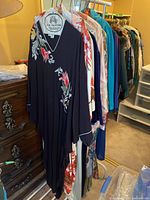 Rack of multiple vintage robes hanging, front view showing black floral robe and white/red scenic print robe