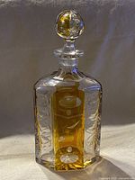 Front view of decanter with stopper on, showing gold-colored panels and detailed cut glass patterns.